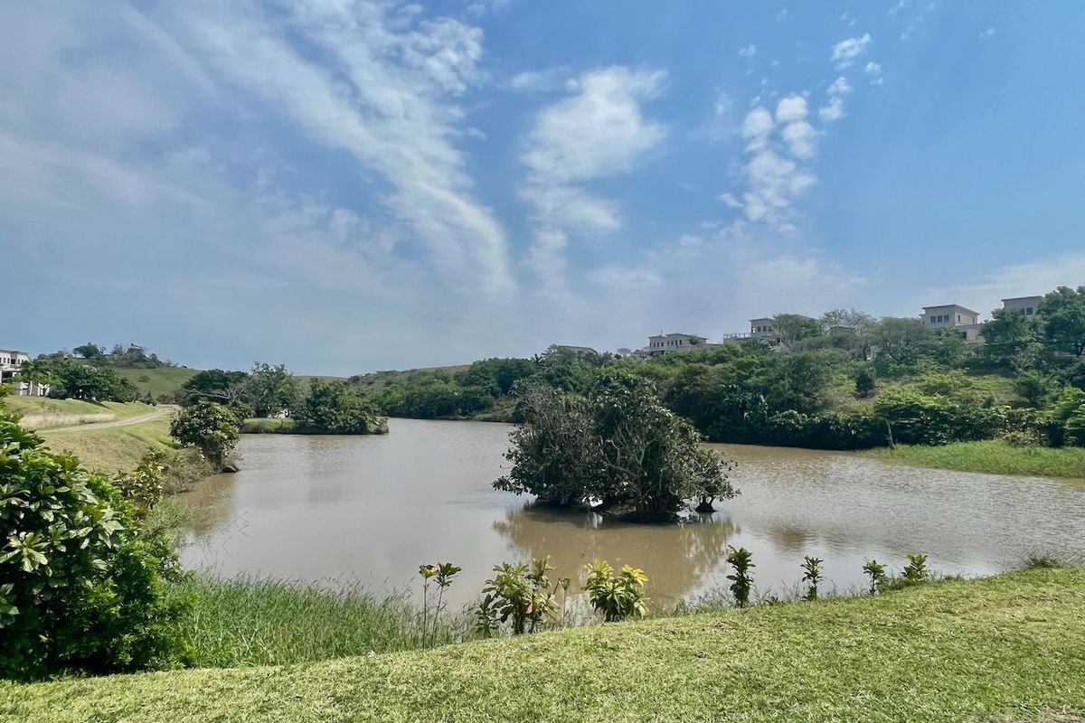 A scenic view of a tranquil lake surrounded by lush greenery and distant residential properties, showcasing the natural landscape of the estate.
