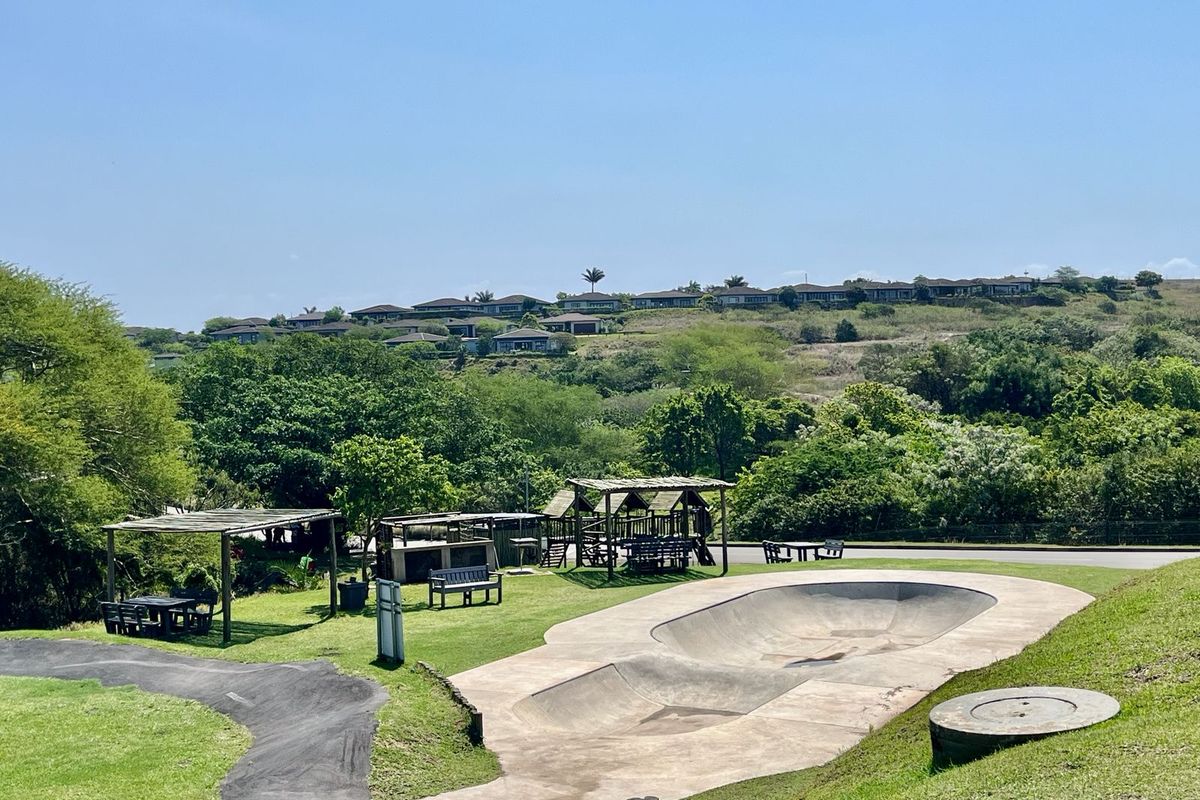 Outdoor recreational area featuring a concrete skate bowl, paved pathways, and shaded timber pergolas set within a landscaped community environment.