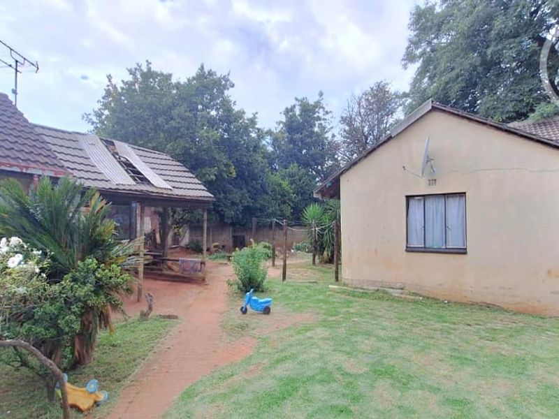 Rear view of the property showing a garden area, tiled roof structures, and exterior walls requiring maintenance and repair.