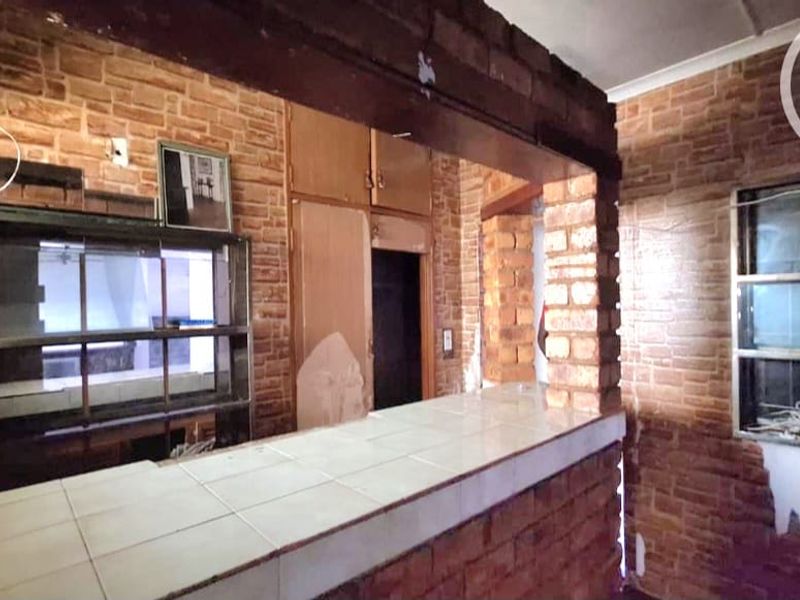 A dated kitchen area featuring exposed brick walls, a tiled breakfast bar, and built-in cabinetry, requiring renovation to modernize the space.
