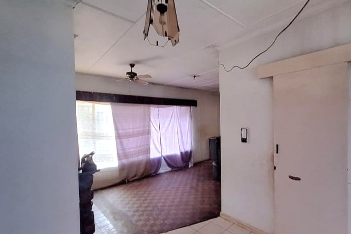 An empty living room featuring tiled flooring, a ceiling fan, and a sliding door, requiring cosmetic updates and repairs to the ceiling and wiring.