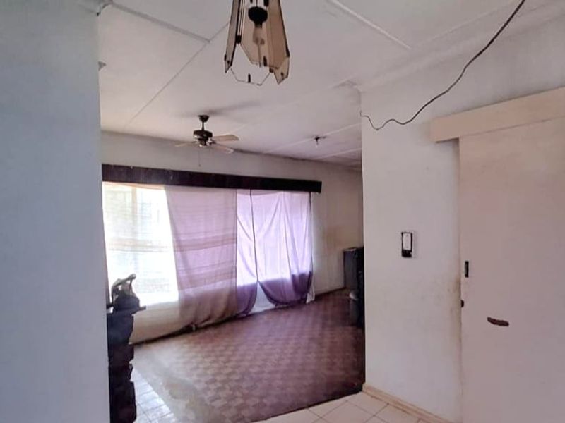 An empty living room featuring tiled flooring, a ceiling fan, and a sliding door, requiring cosmetic updates and repairs to the ceiling and wiring.
