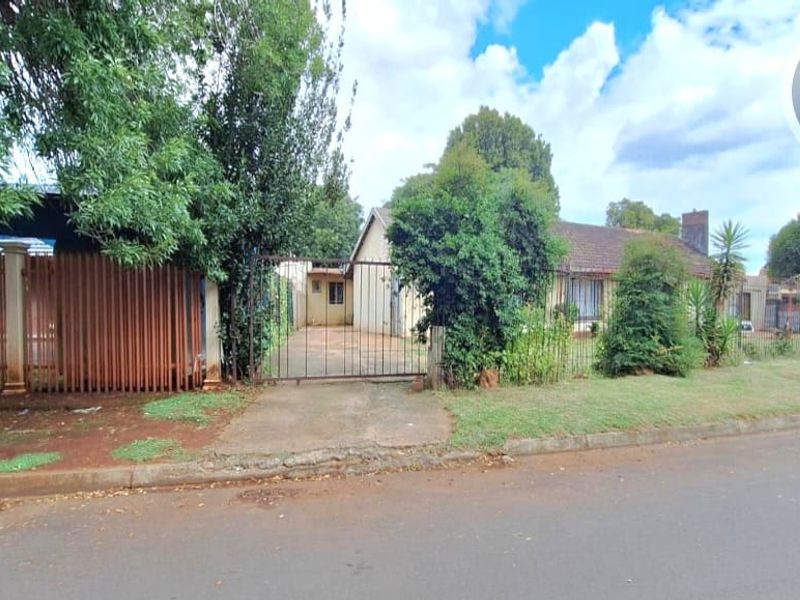 Front view of a residential property featuring a gated driveway, perimeter fencing, and a tiled roof structure with a brick chimney.