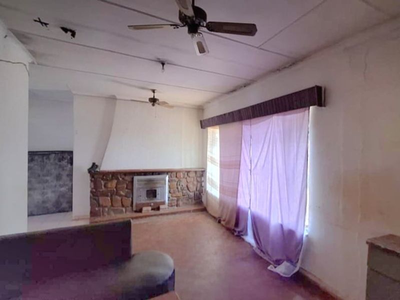 Living room featuring a stone fireplace with a built-in insert, ceiling fans, and significant signs of wear on the walls and ceiling.