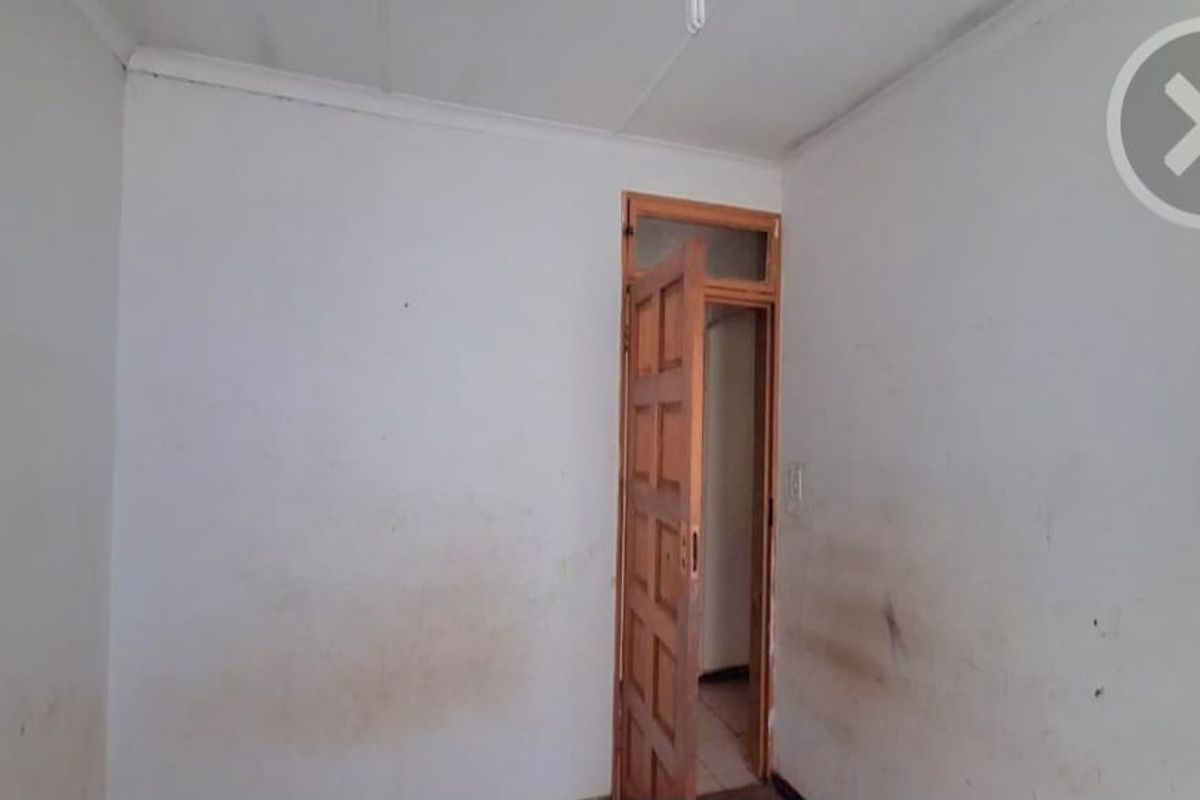 An empty bedroom featuring a timber door with a transom window, requiring cosmetic updates to the wall finishes.