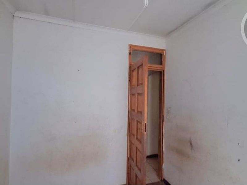 An empty bedroom featuring a timber door with a transom window, requiring cosmetic updates to the wall finishes.