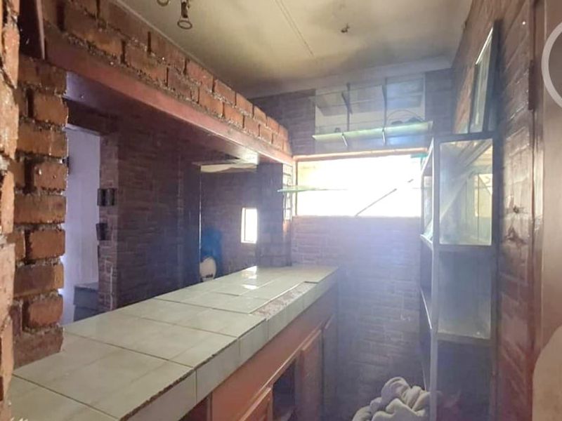 A rustic bar area featuring exposed brick walls, a tiled counter, and built-in glass shelving, offering potential for a modern entertainment space renovation.