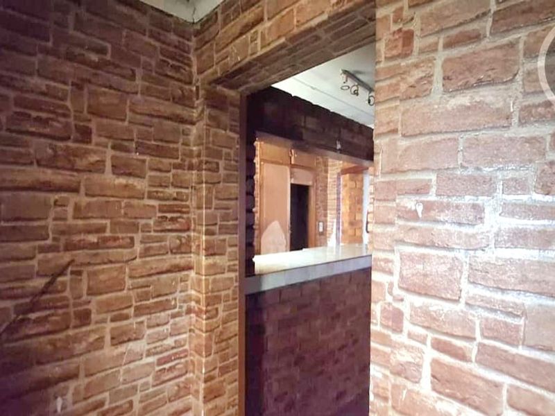 A hallway featuring dated brick-style wall cladding and a pass-through opening looking into an adjacent room with a countertop.