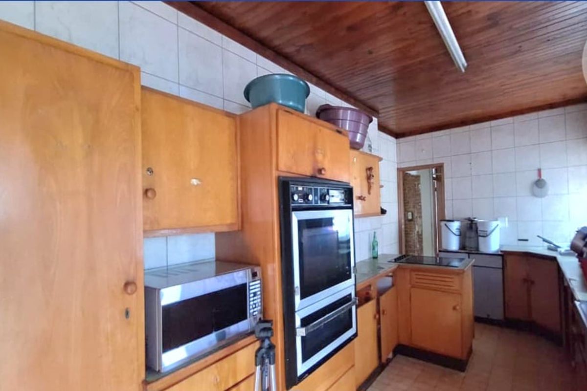 A dated kitchen featuring original wooden cabinetry, a built-in double oven, tiled splashbacks, and a timber-paneled ceiling.