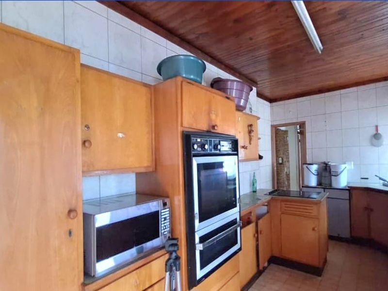 A dated kitchen featuring original wooden cabinetry, a built-in double oven, tiled splashbacks, and a timber-paneled ceiling.