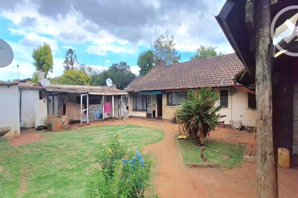 Rear view of the property featuring a garden, brick paved pathways, and a covered patio area with an adjacent outbuilding.