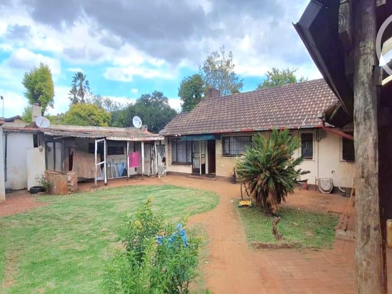 Rear view of the property featuring a garden, brick paved pathways, and a covered patio area with an adjacent outbuilding.