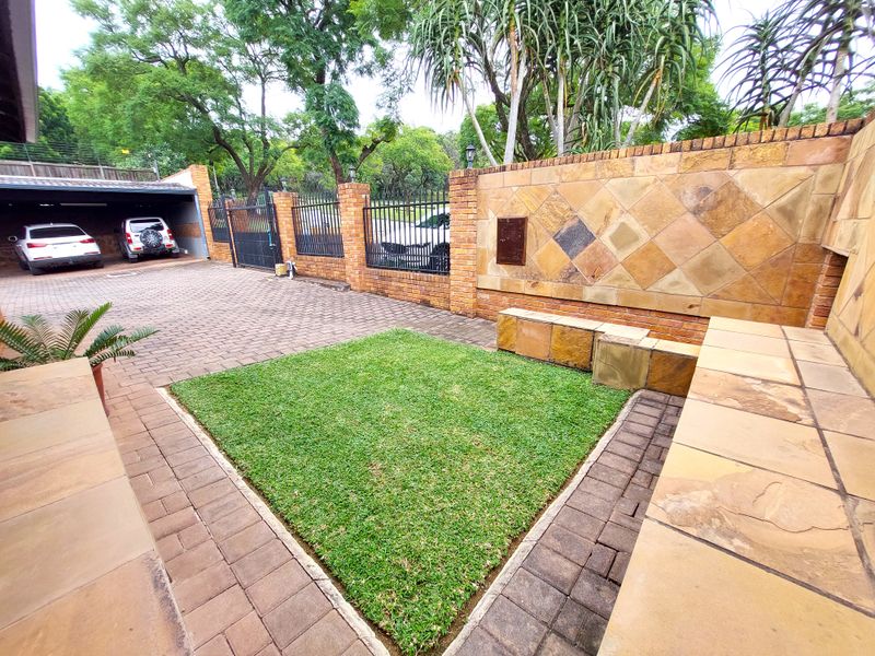 Front courtyard area featuring brick paving, a manicured lawn patch, stone-clad feature wall with built-in seating, and a covered carport.
