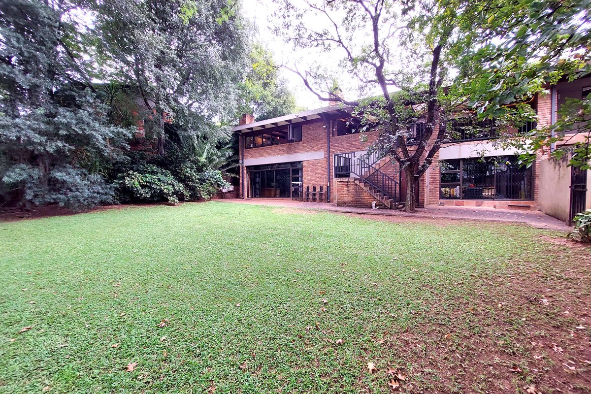 Spacious rear garden featuring a large lawn, mature trees, and a two-story brick residence with an external staircase and sliding door access.