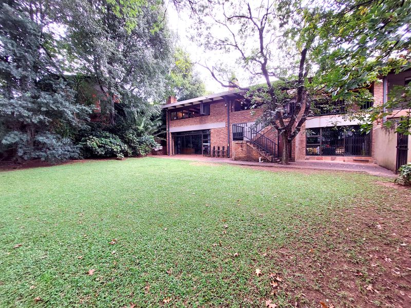 Spacious rear garden featuring a large lawn, mature trees, and a two-story brick residence with an external staircase and sliding door access.