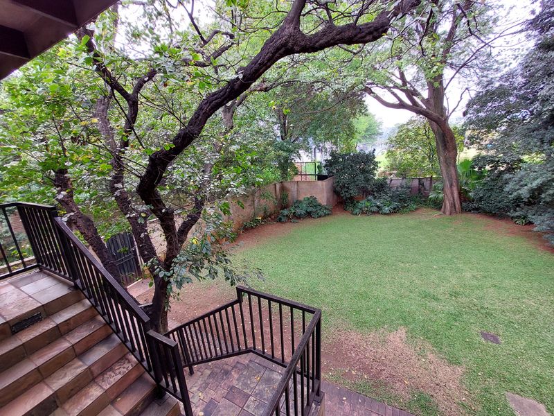 A view of the rear garden featuring a tiled staircase with metal railings leading down to a spacious lawn area surrounded by mature trees.