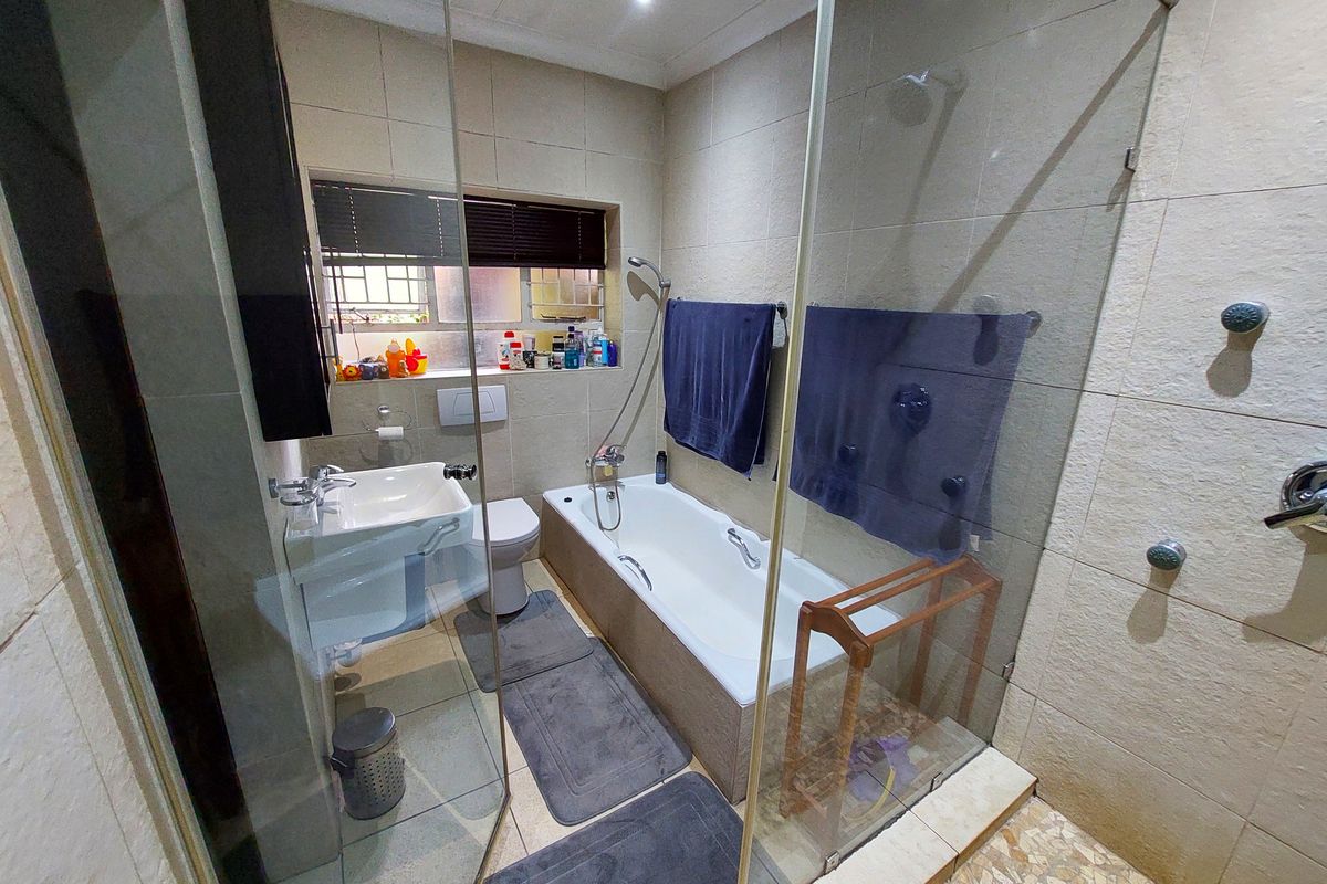 A functional bathroom featuring a bathtub, glass-enclosed shower, wall-mounted basin, and toilet with neutral wall and floor tiling.