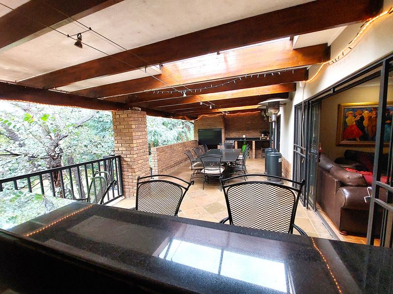 Spacious covered patio featuring exposed timber beams, stone flooring, and a built-in brick braai area, perfect for outdoor entertaining.