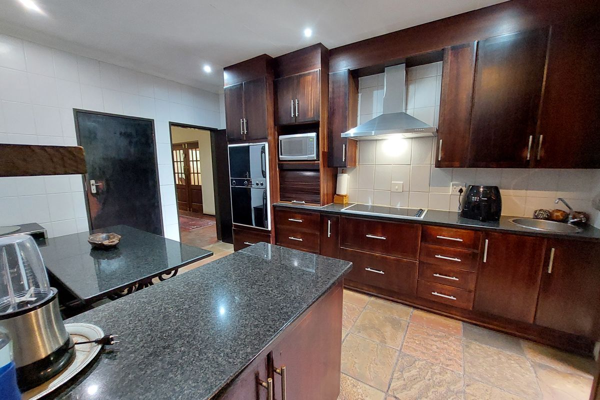 A well-appointed kitchen featuring dark wood cabinetry, granite countertops, built-in appliances, and durable stone tile flooring.