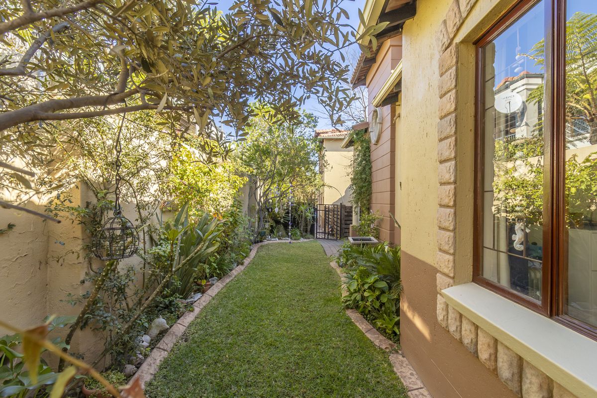 A well-maintained rear garden featuring a manicured lawn, stone-accented exterior wall, and a paved pathway leading to a secure metal gate.