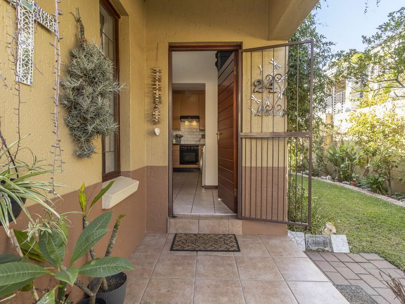 A welcoming front entrance featuring a tiled porch, security gate, and timber door, providing a clear view into the kitchen area.