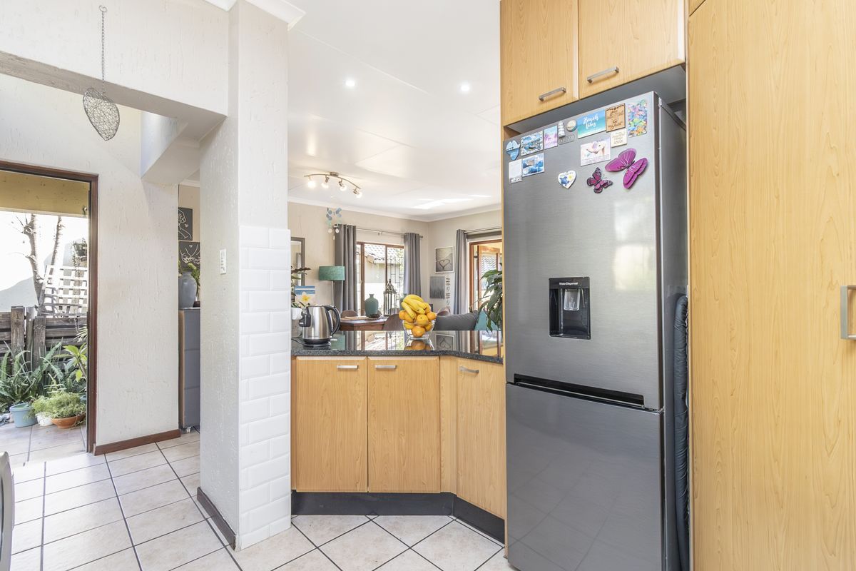 A functional kitchen featuring light wood cabinetry, granite countertops, and tiled flooring, with an open-plan flow into the adjacent living area.
