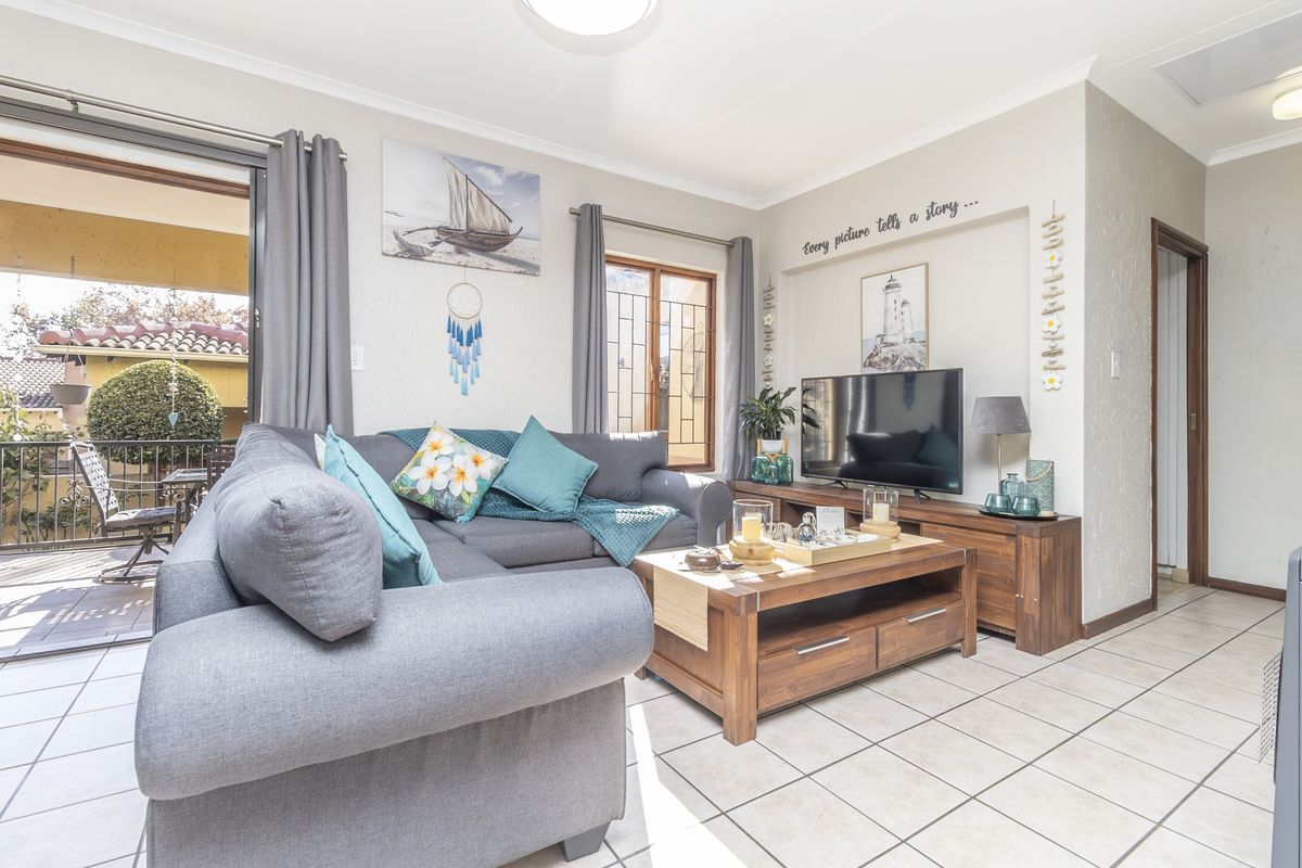 A bright and well-maintained living room featuring tiled flooring and a sliding glass door providing access to an outdoor patio area.