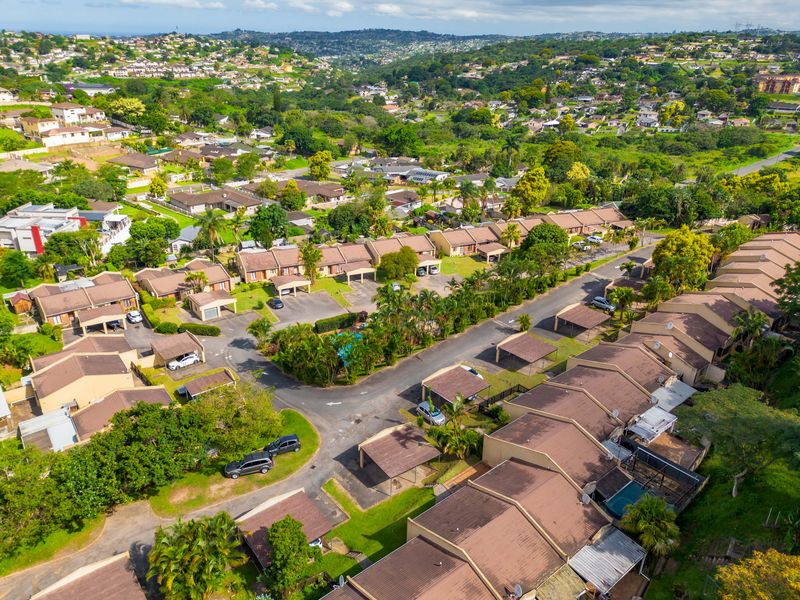 An aerial view of a residential townhouse complex featuring tiled roof units, private carports, and a communal swimming pool set within a landscaped estate.