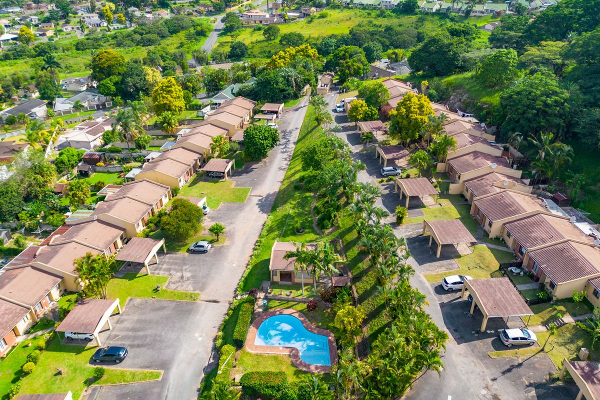 Aerial view of a residential townhouse complex featuring multiple units, private carports, landscaped communal grounds, and a central swimming pool.