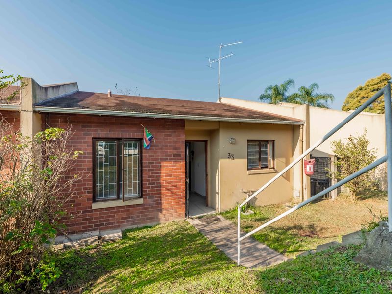 Front elevation of a single-story townhouse featuring a brick and plaster facade, concrete walkway, and metal security features.