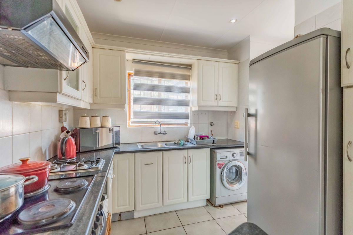 A functional kitchen featuring white cabinetry, dark countertops, a gas hob with extractor, and integrated laundry plumbing, offering a practical layout for daily use.