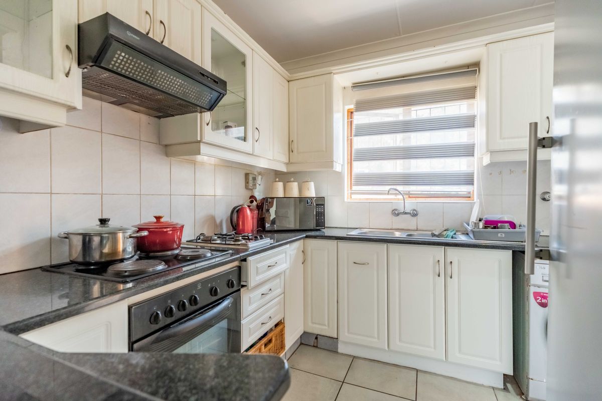 A functional kitchen featuring white cabinetry, dark countertops, a built-in oven with hob, extractor fan, and a double sink with tiled backsplash.