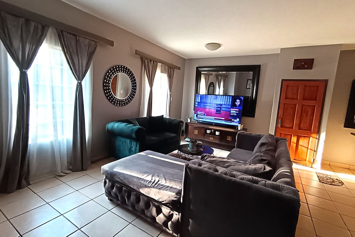 A living room featuring tiled flooring, a large wall mirror, and a wooden entrance door, providing a functional and comfortable living space.