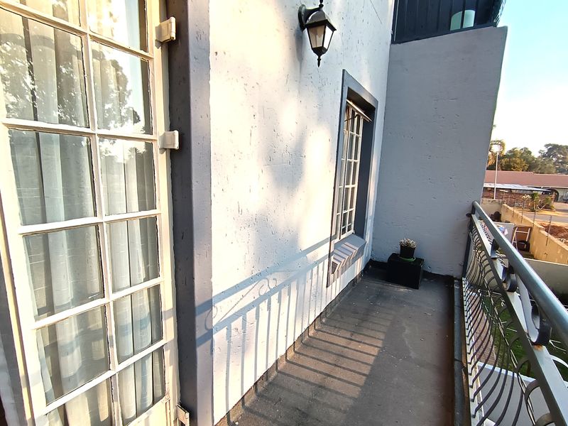 A balcony area featuring a wrought iron balustrade, exterior wall lighting, and access via french doors, showing signs of wear on the floor and railing.