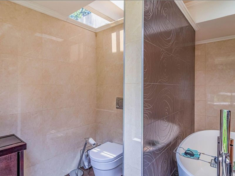 Modern bathroom featuring a freestanding bathtub, wall-mounted toilet, and a skylight, complemented by decorative feature tiling.