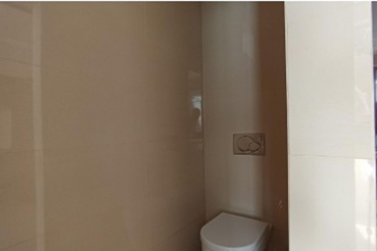 A compact bathroom featuring a wall-mounted toilet with a modern flush plate and neutral wall tiling.