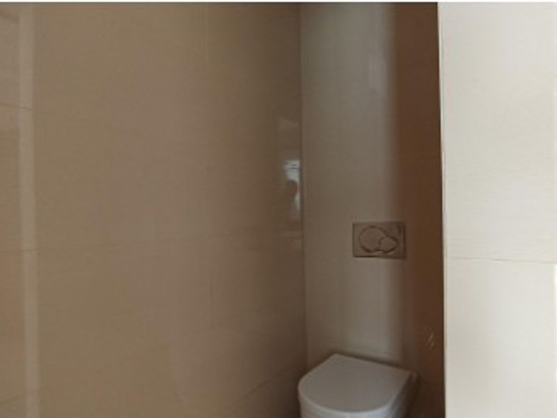 A compact bathroom featuring a wall-mounted toilet with a modern flush plate and neutral wall tiling.
