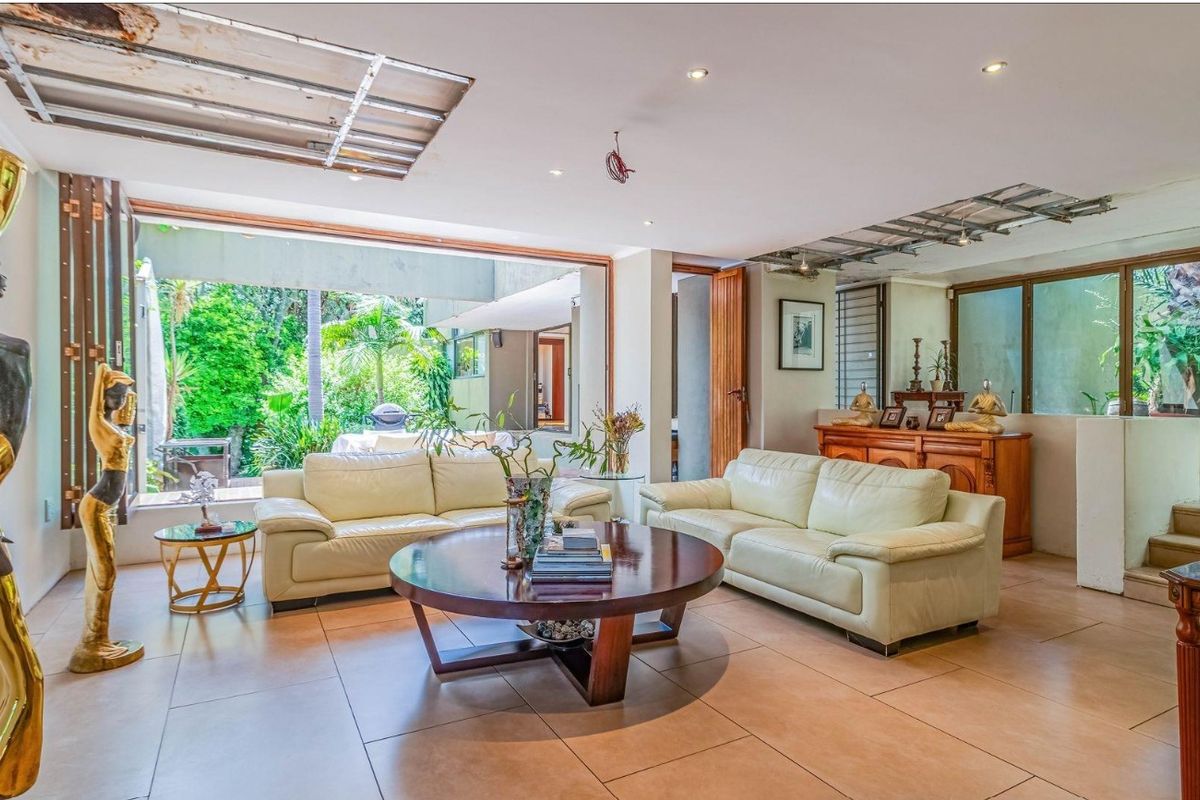 Spacious living room with large sliding doors opening to the garden, featuring tiled floors and recessed lighting, currently requiring ceiling repairs.