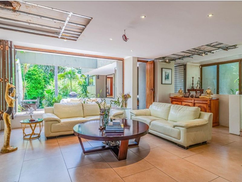 Spacious living room with large sliding doors opening to the garden, featuring tiled floors and recessed lighting, currently requiring ceiling repairs.