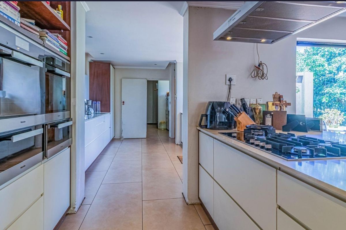 Modern kitchen featuring built-in appliances, gas hob, extractor fan, and ample cabinetry with stone countertops, leading into a hallway.
