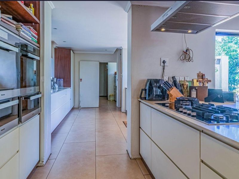 Modern kitchen featuring built-in appliances, gas hob, extractor fan, and ample cabinetry with stone countertops, leading into a hallway.
