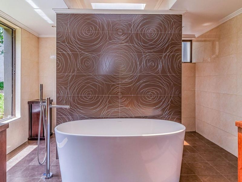 Modern bathroom featuring a central freestanding bathtub, a decorative tiled feature wall, and a skylight providing natural light.