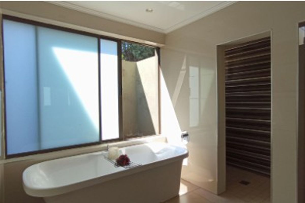 Modern bathroom featuring a sleek freestanding bathtub, large frosted window for natural light, and a separate walk-in shower area with decorative tiled accents.