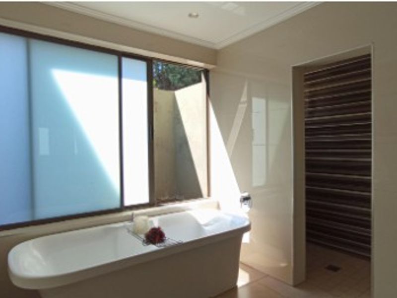 Modern bathroom featuring a sleek freestanding bathtub, large frosted window for natural light, and a separate walk-in shower area with decorative tiled accents.