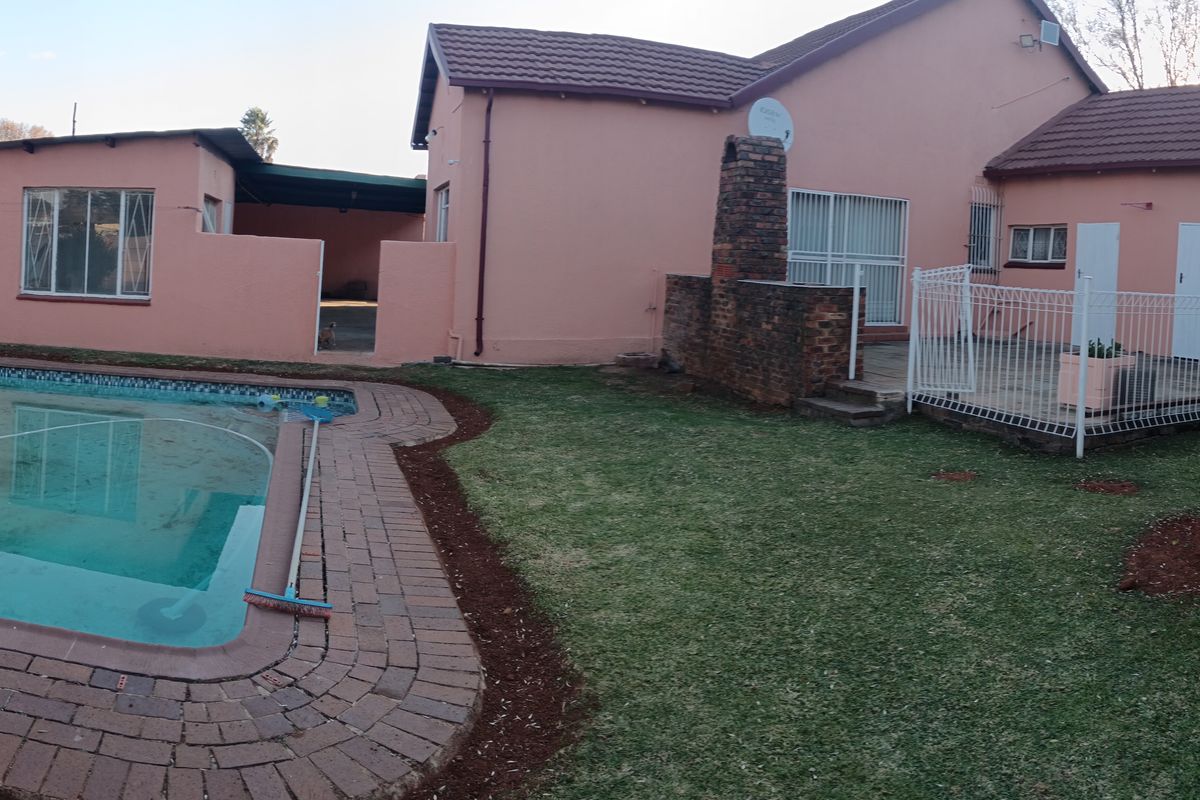 Rear exterior view featuring a swimming pool, brick patio area with a built-in fireplace, and a large garden space with boundary walls.