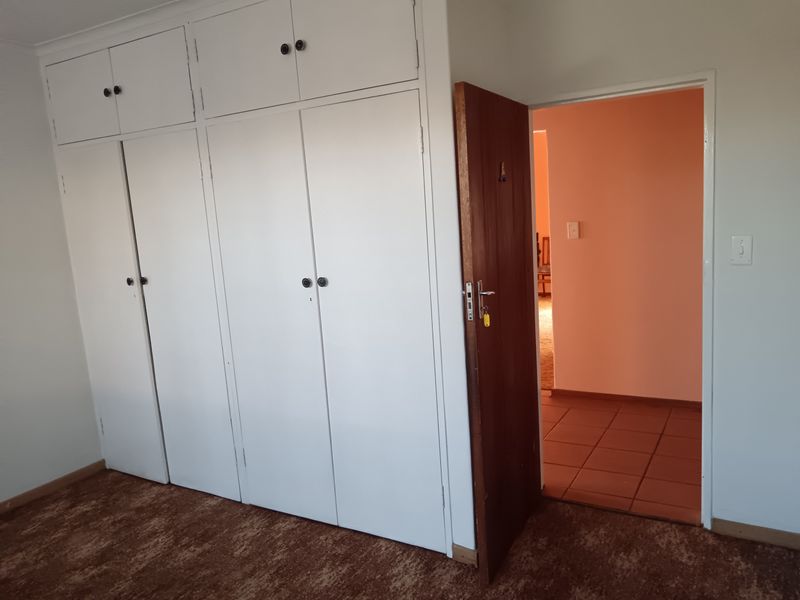 A bedroom featuring extensive built-in cupboards with overhead storage and a wooden door leading to an adjacent tiled hallway.