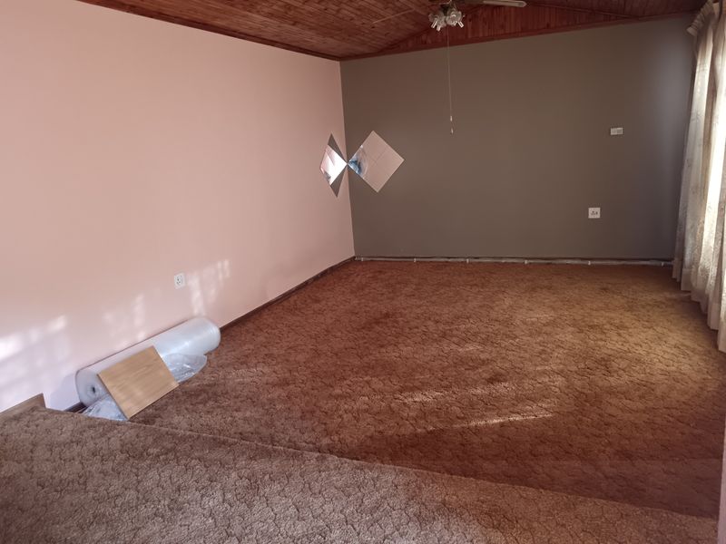 Spacious living area featuring a timber-clad ceiling, ceiling fan, and carpeted flooring, offering a blank canvas for renovation.