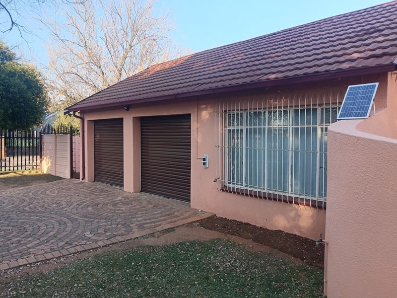 Front view of the property featuring a double garage with roller shutter doors, paved driveway, and security bars on the windows.