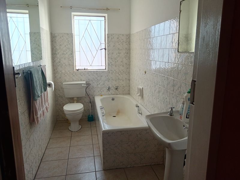A dated bathroom featuring a standard bathtub, pedestal basin, and toilet with original ceramic wall and floor tiling.