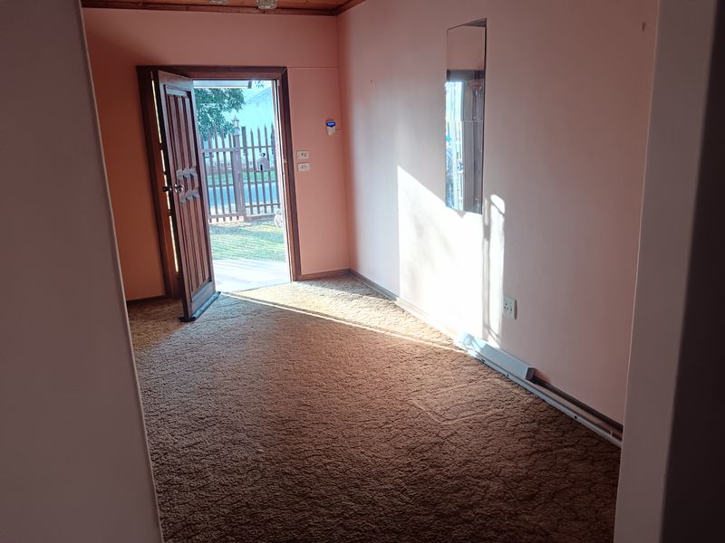 An empty entry area featuring carpet flooring, a timber door, and a wall-mounted mirror, providing direct access to the exterior.
